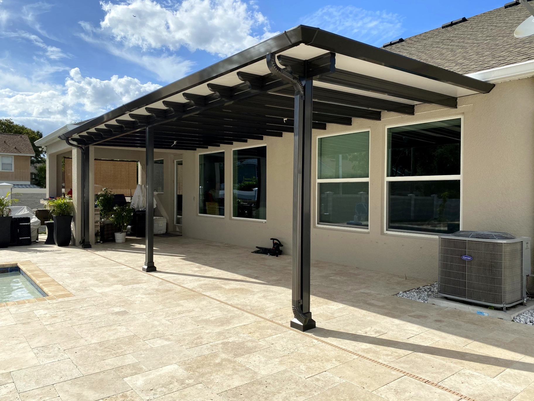 Aluminum patio cover over a travertine pool deck on a sunny day — Tampa Bay, Florida